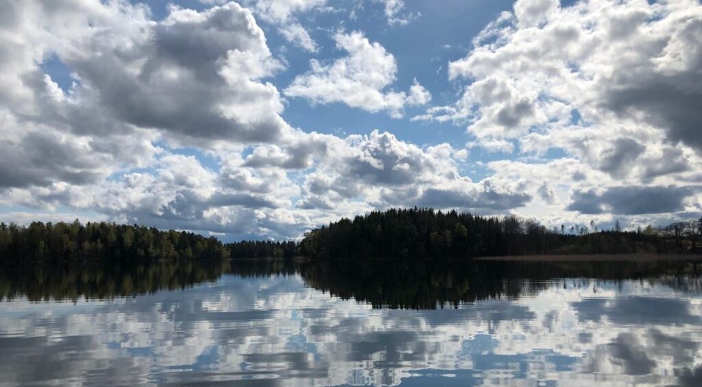 En stilla vattenyta som gör att molnen på himlen speglar sig i vattnet.