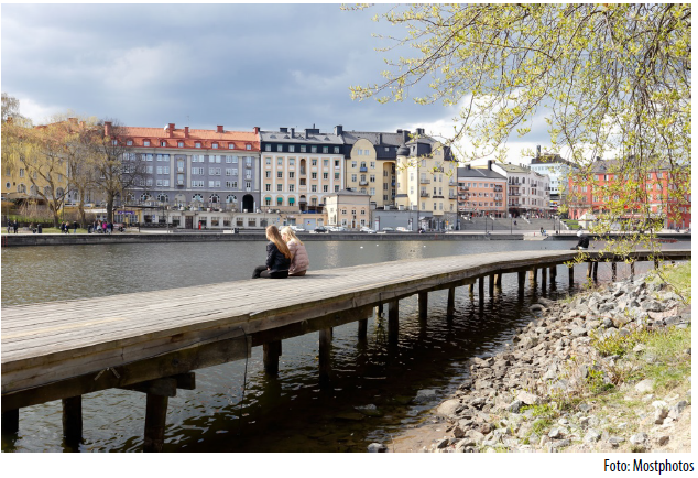 Två personer sitter på en träbrygga i en stor stad.